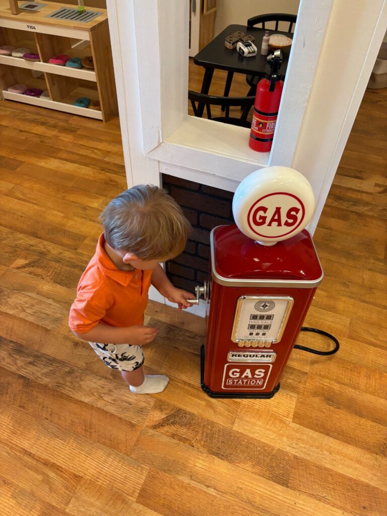 Toddler using a toy gas station pump during imaginative playtime at Mama Bear’s Play Cafe in Northern Colorado.
