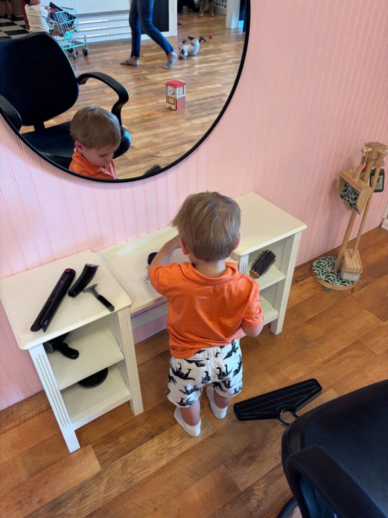 Toddler playing at the pretend hair salon station inside Mama Bear’s Play Cafe in Loveland, Colorado.